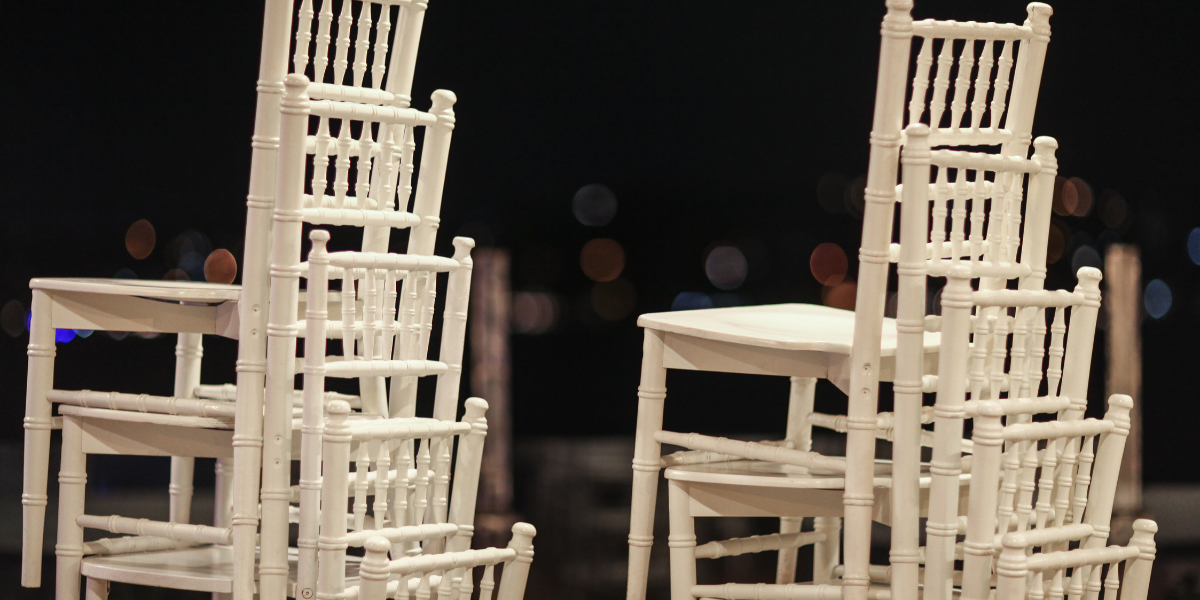 Stacked white chiavari chairs silhouetted against blurred city lights at night