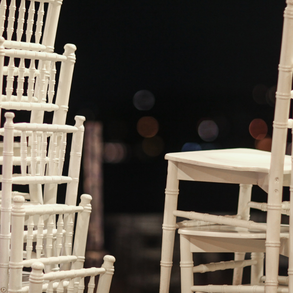 Stacked white chiavari chairs silhouetted against blurred city lights at night