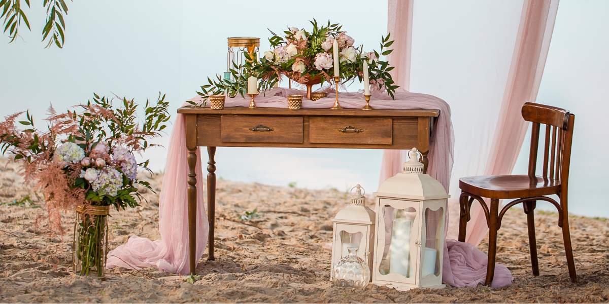 Beachside wedding welcome table decorated with pink drapery, candles, and flowers