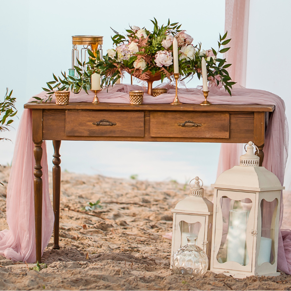 Beachside wedding welcome table decorated with pink drapery, candles, and flowers