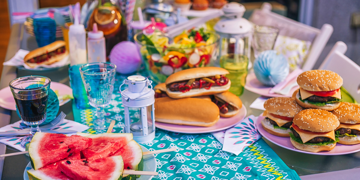 Backyard barbecue spread of burgers, hot dogs, watermelon, and salad on a table