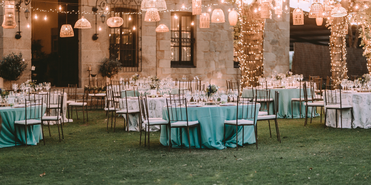Outdoor evening reception with teal linens, chiavari chairs, and hanging woven lights