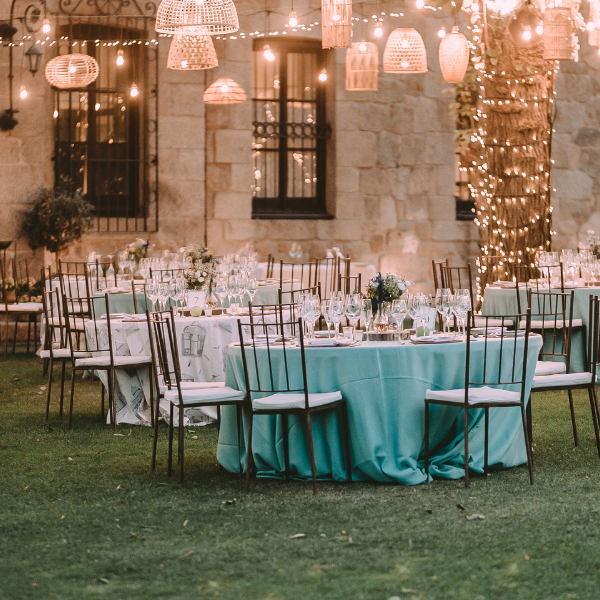 Outdoor evening reception with teal linens, chiavari chairs, and hanging woven lights