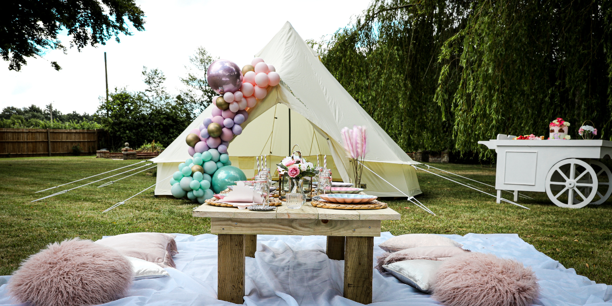 Cream bell tent decorated with a pastel balloon garland in a garden picnic setup