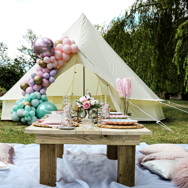 Cream bell tent decorated with a pastel balloon garland in a garden picnic setup