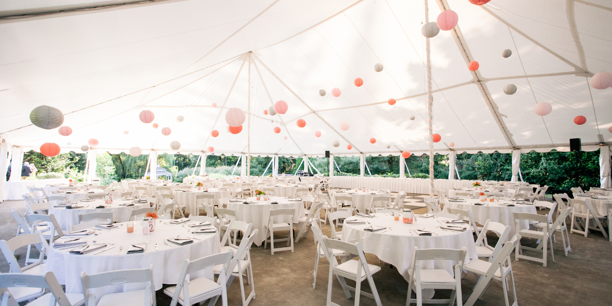 Tent interior hung with round paper lanterns over tables set for a reception dinner