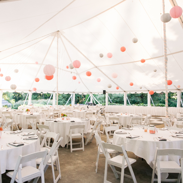 Tent interior hung with round paper lanterns over tables set for a reception dinner