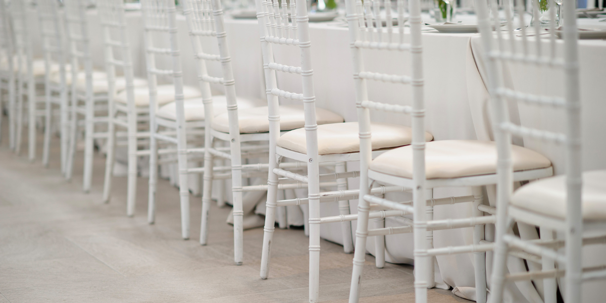 Close-up row of white chiavari chairs with cream cushions along a linen-covered table