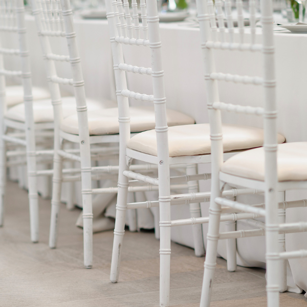 Close-up row of white chiavari chairs with cream cushions along a linen-covered table