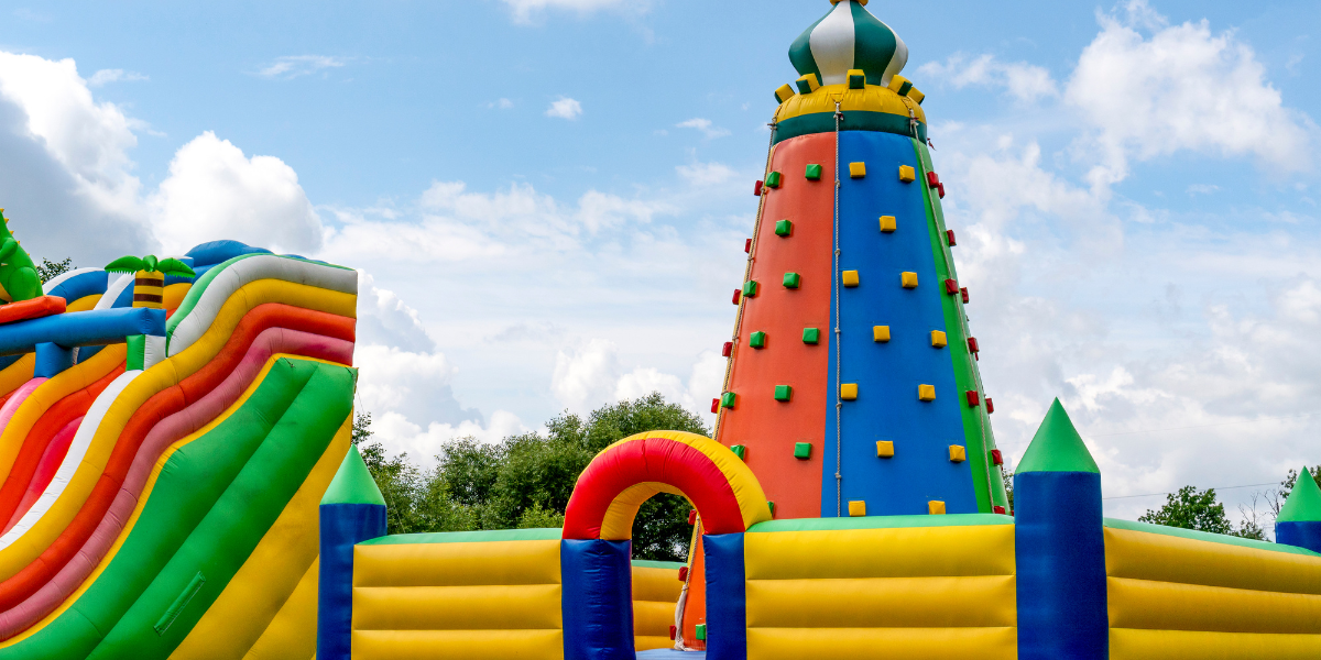 Colorful inflatable play structure with a tall rock-climbing tower and striped slide