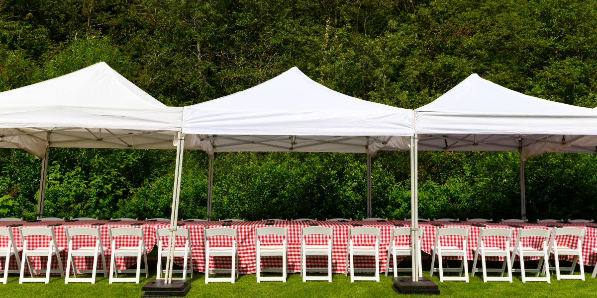 Three connected white pop-up tents over tables draped in red and white checkered linens