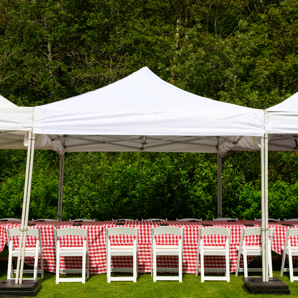Three connected white pop-up tents over tables draped in red and white checkered linens