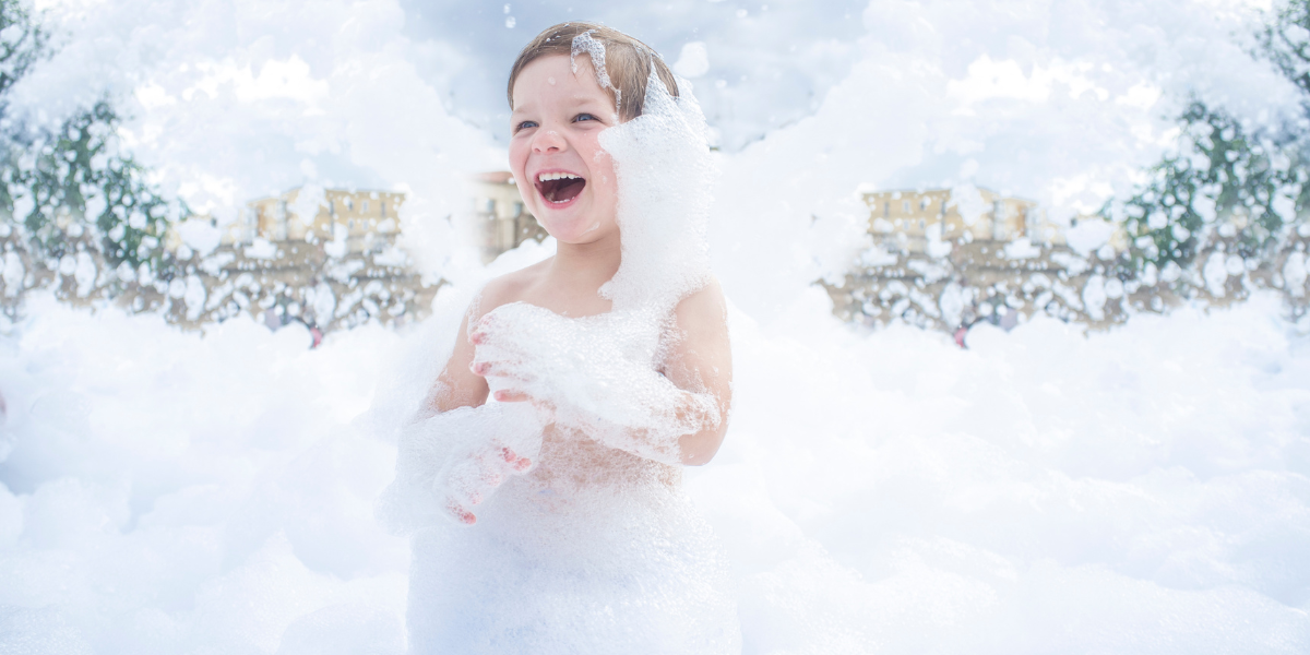 Child covered head to toe in white foam from an outdoor foam party machine