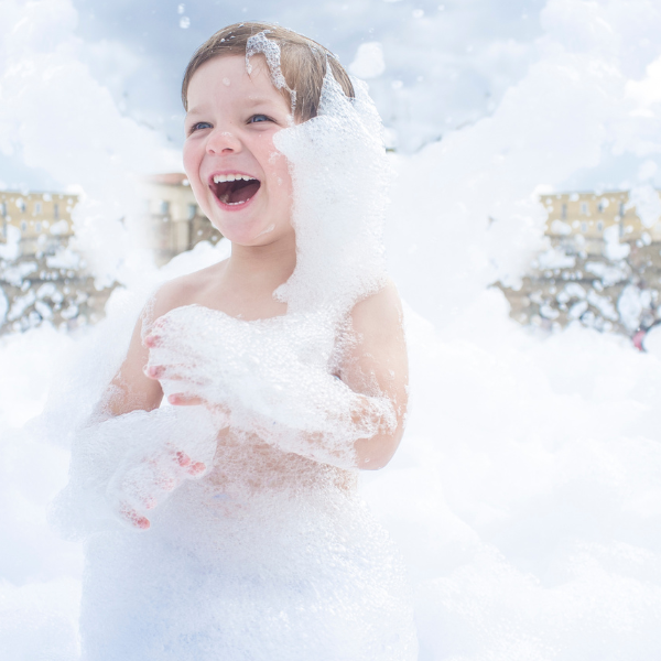 Child covered head to toe in white foam from an outdoor foam party machine