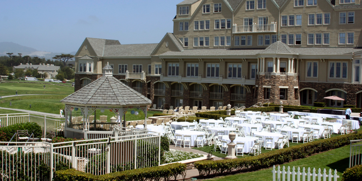 Large resort building with round tables and white folding chairs set up on a lawn terrace