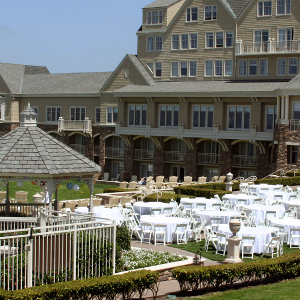 Large resort building with round tables and white folding chairs set up on a lawn terrace