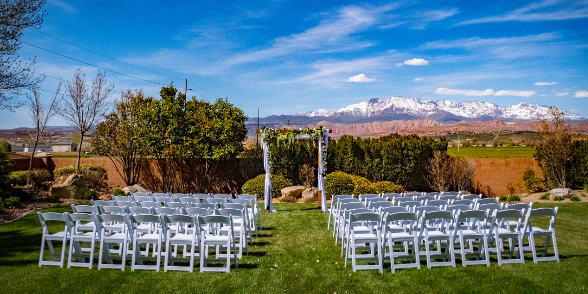 Rows of white folding chairs set for an outdoor wedding with snow-capped mountains behind