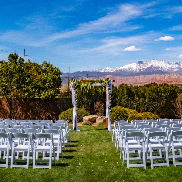 Rows of white folding chairs set for an outdoor wedding with snow-capped mountains behind