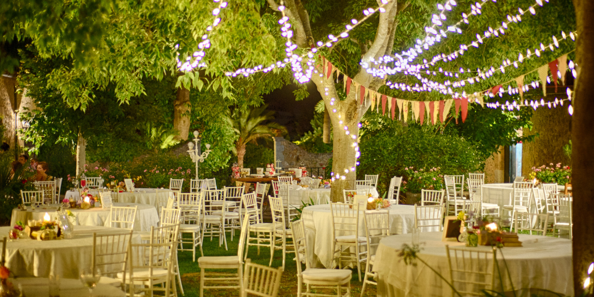 Outdoor garden party at night under trees strung with fairy lights and pennant bunting