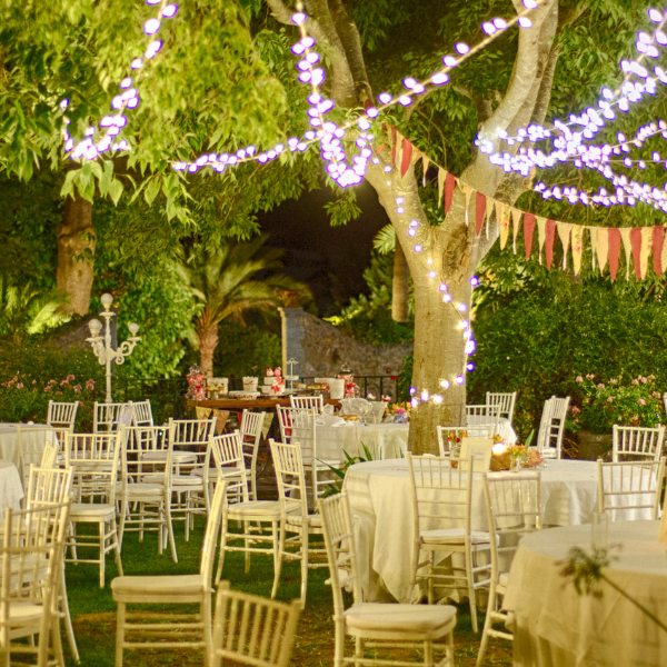 Outdoor garden party at night under trees strung with fairy lights and pennant bunting