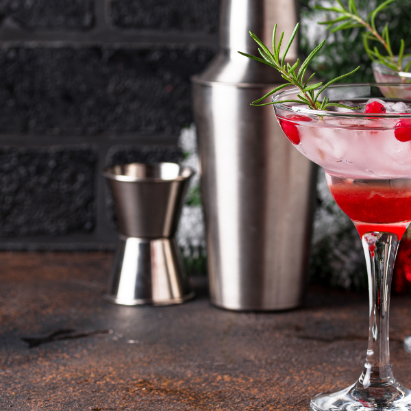 Two cranberry cocktails garnished with rosemary sprigs beside holiday pine decor