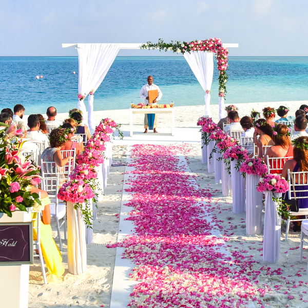 Beach wedding ceremony with a petal-strewn aisle, white chairs, and an ocean backdrop