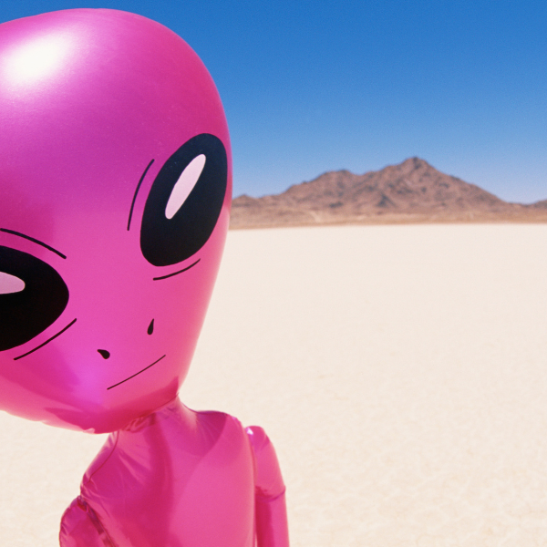 Pink inflatable alien figure standing on a flat desert salt pan with mountains behind