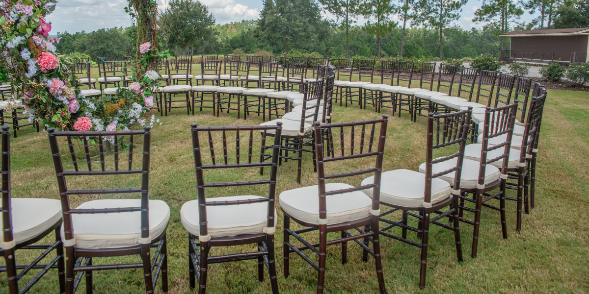 Rows of dark wood chiavari chairs with cream cushions curve around an outdoor ceremony