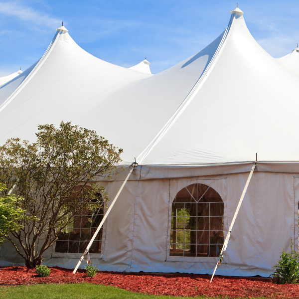 Peaked white pole tent with cathedral-window sidewalls on a landscaped lawn