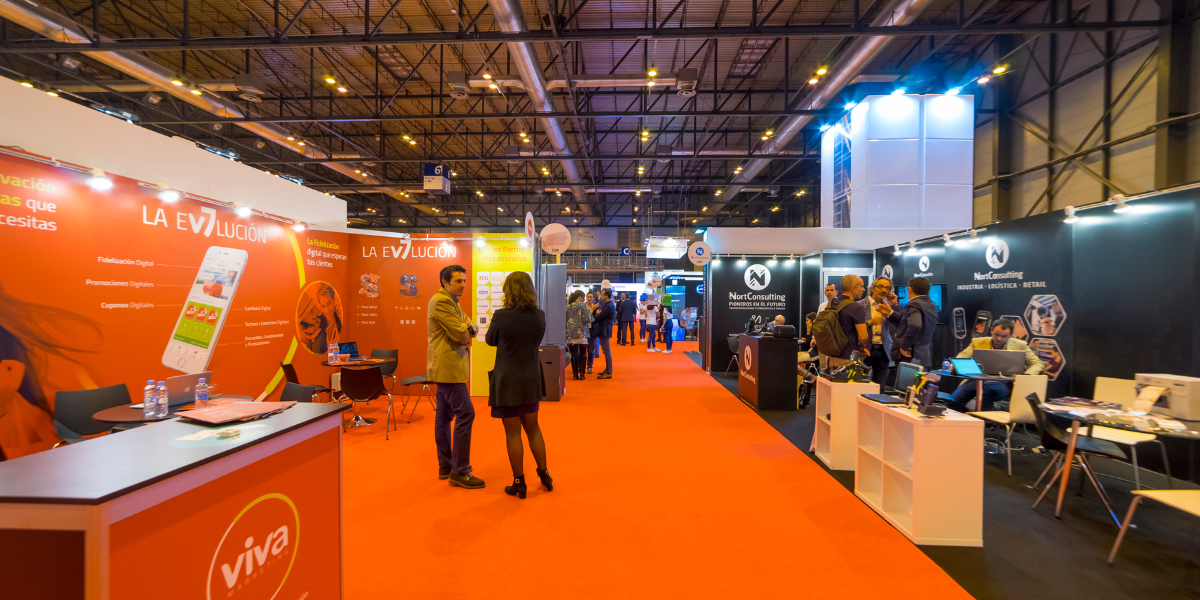 Indoor trade show hall with orange carpeted aisle flooring and branded exhibitor booths