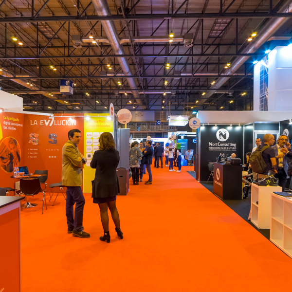 Indoor trade show hall with orange carpeted aisle flooring and branded exhibitor booths