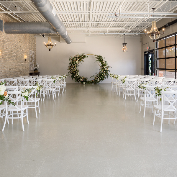 Industrial-style venue with exposed brick set up for a wedding ceremony with white chairs