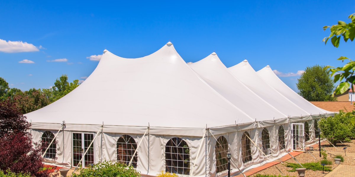 Large multi-peak white pole tent with cathedral windows on a sunny landscaped lawn