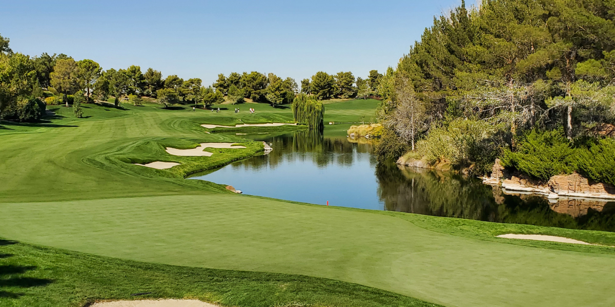 Golf course fairway with sand bunkers and a pond reflecting trees under a blue sky