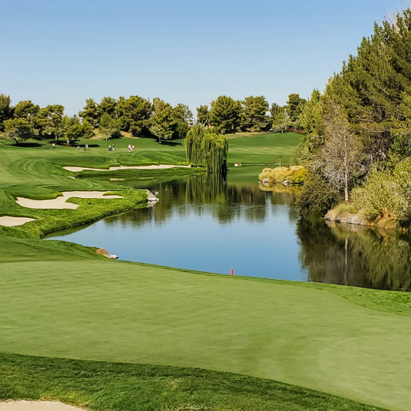 Golf course fairway with sand bunkers and a pond reflecting trees under a blue sky
