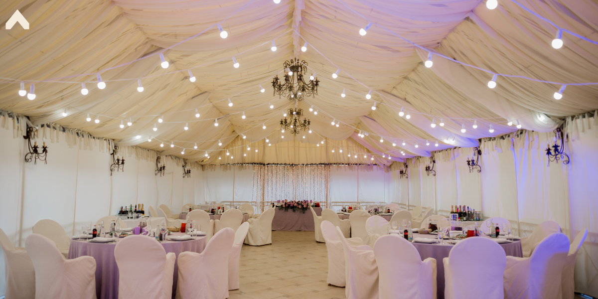Fabric-draped tent interior lit by chandeliers and string lights, set for a wedding dinner