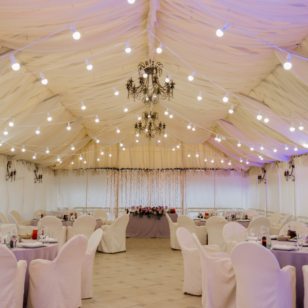 Fabric-draped tent interior lit by chandeliers and string lights, set for a wedding dinner