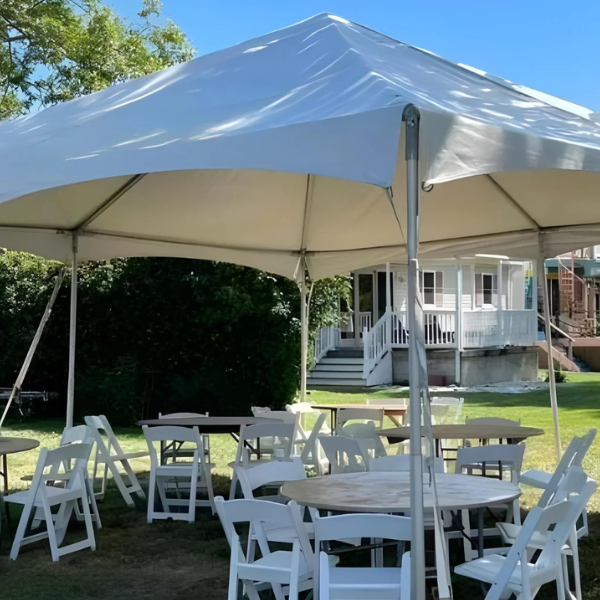 White frame tent shading round tables and folding chairs in a sunny backyard
