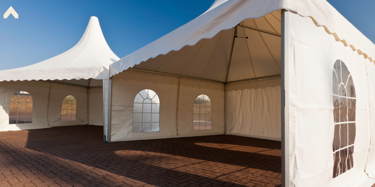 Empty white marquee tents with arched cathedral windows set up on a sunny brick patio