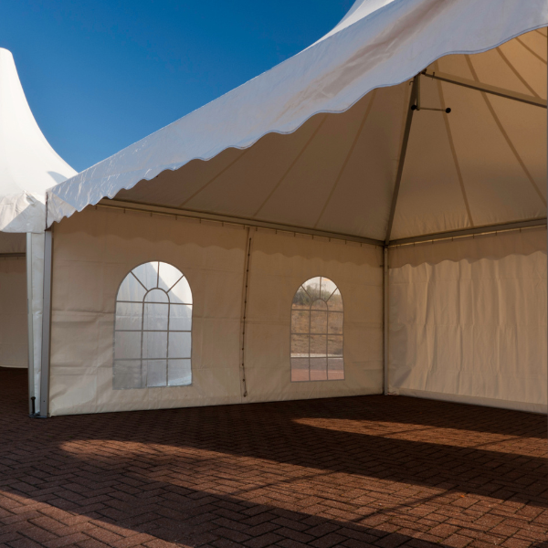 Empty white marquee tents with arched cathedral windows set up on a sunny brick patio