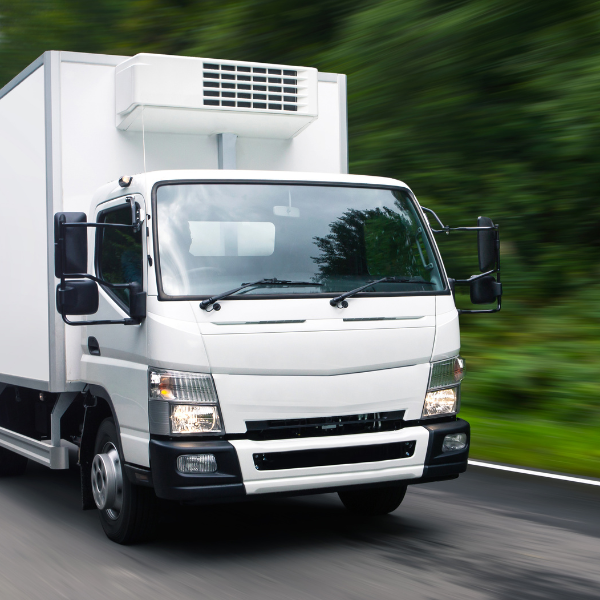 White box truck with a refrigerated cargo body driving along a forest-lined road