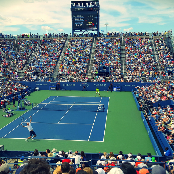 Packed tennis stadium crowd watching two players rally on a blue and green hard court