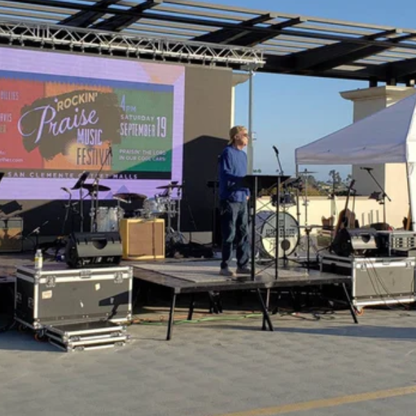 Musician on a raised stage platform with pop-up canopy tents nearby at an outdoor festival