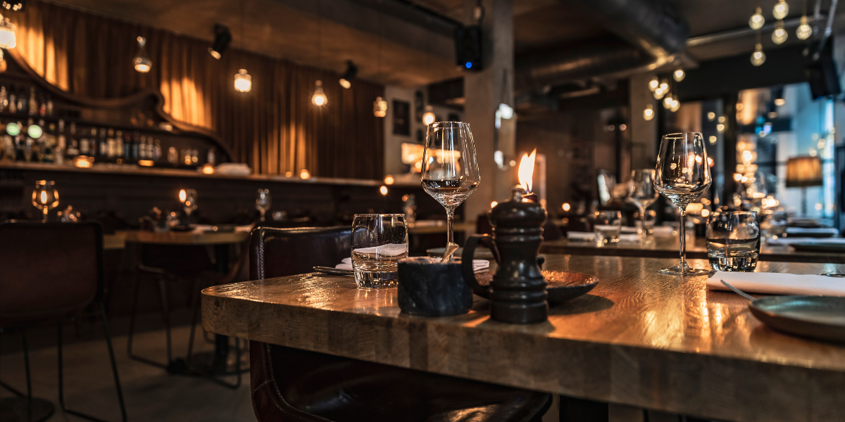 Dimly lit restaurant bar with wine glasses, a candle, and hanging bulb string lights