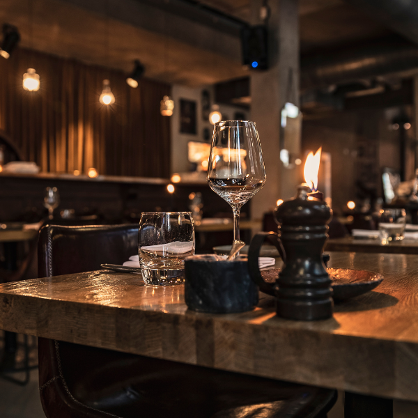 Dimly lit restaurant bar with wine glasses, a candle, and hanging bulb string lights