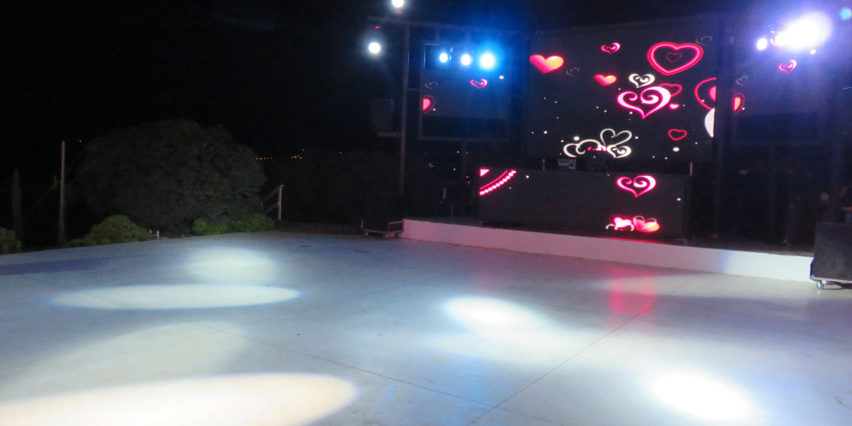 Outdoor nighttime dance floor lit by spotlights in front of an LED screen with heart graphics