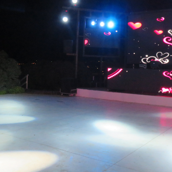 Outdoor nighttime dance floor lit by spotlights in front of an LED screen with heart graphics