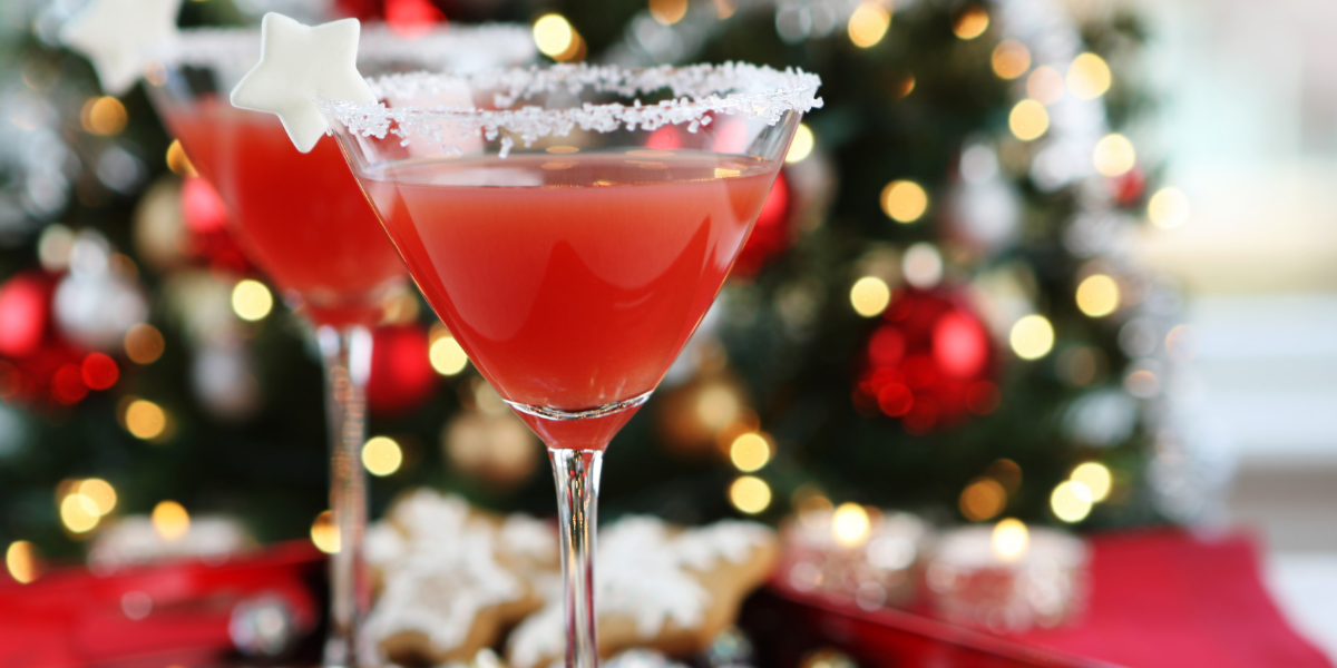 Two red cocktails in sugar-rimmed glasses in front of a blurred Christmas tree