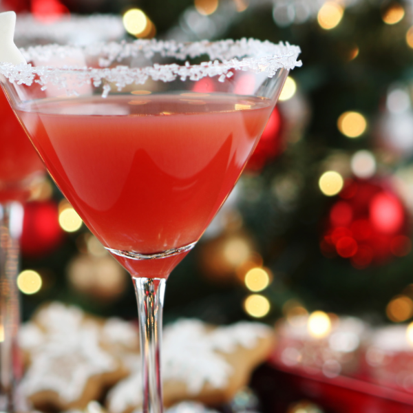 Two red cocktails in sugar-rimmed glasses in front of a blurred Christmas tree