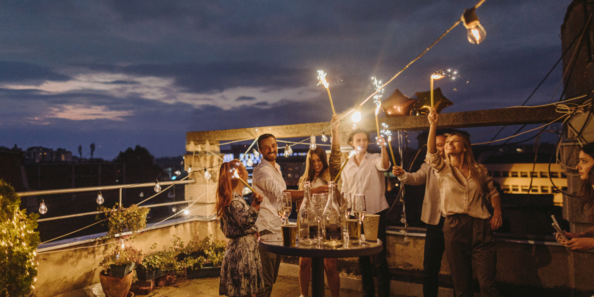 Friends celebrating with sparklers and champagne on a rooftop terrace at night